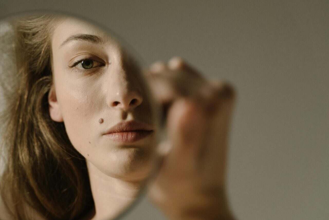 Close-up portrait of a woman looking at her reflection in a round mirror. Soft lighting and selective focus.